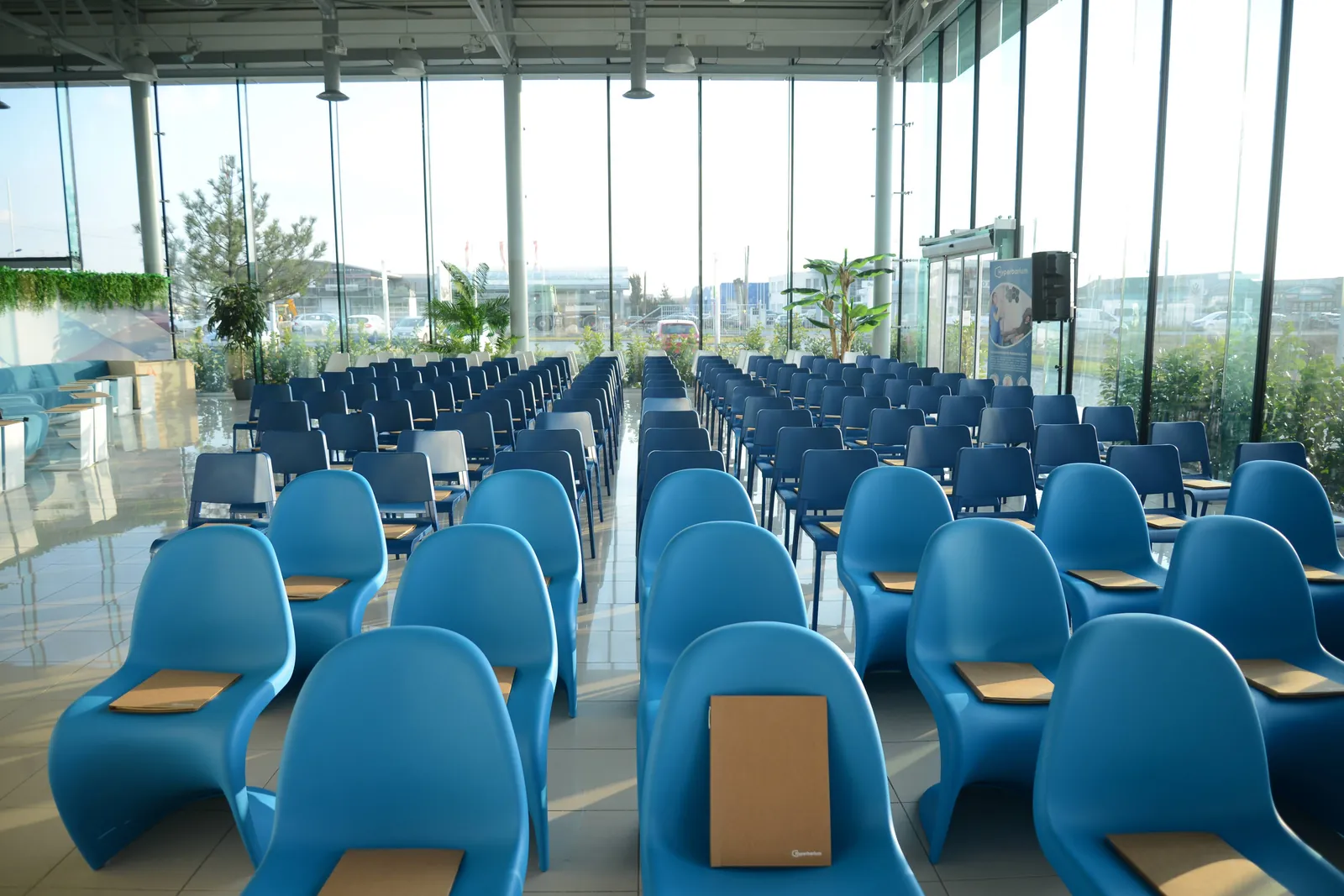The campus event hall arranged theatre-style with rows of blue chairs, floor-to-ceiling glazing, and daylight throughout